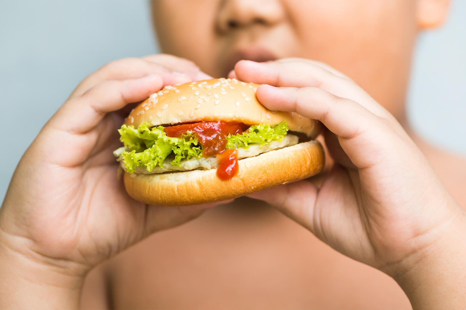 example of child overeating overweight child holding a burger displaying victim of overnutrition