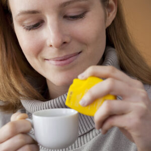 women pouring artificial sweetener in her coffee