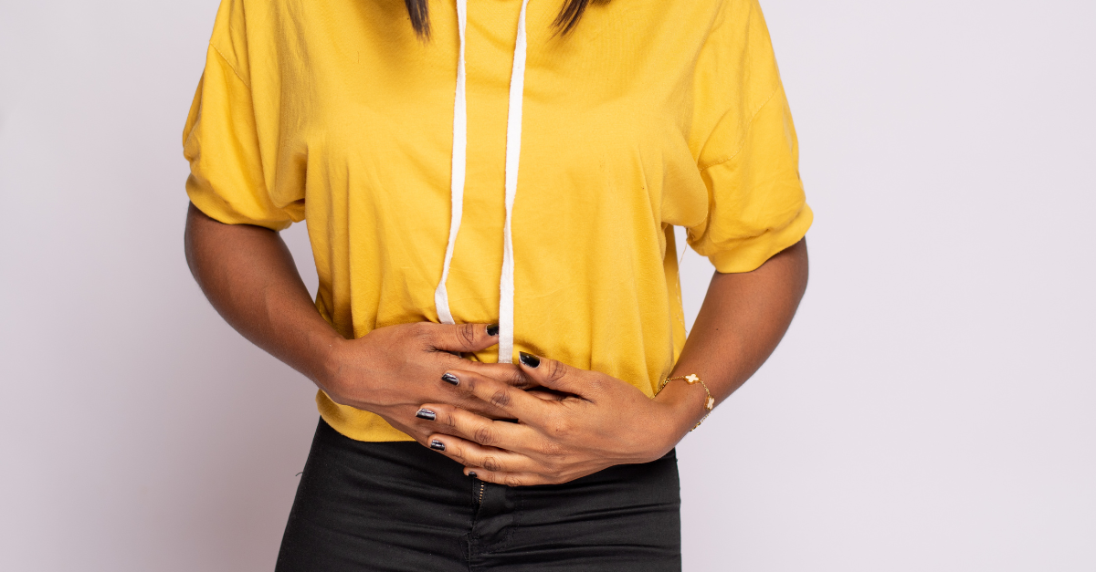 woman in a yellow hoodie holding her stomach in pain due to IBS