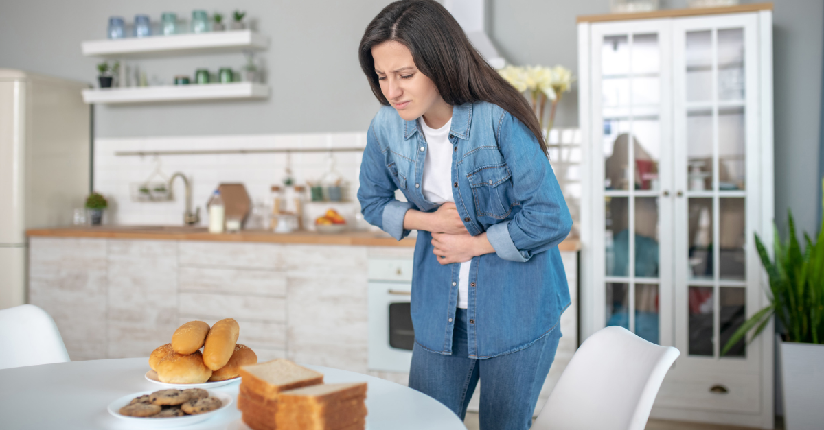 woman holding stomach after eating bread on the table