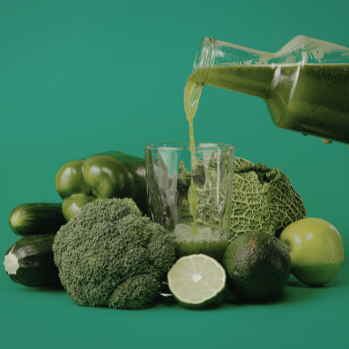 green plant-based smoothie being poured into a glass with fresh ingredients in the background